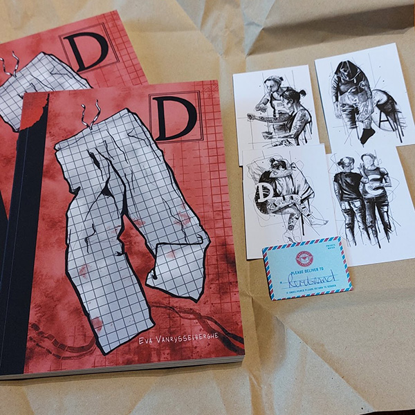 photo of 2 copies of the graphic novel ‘D’ along with some art cards showing figures drawn in black and white