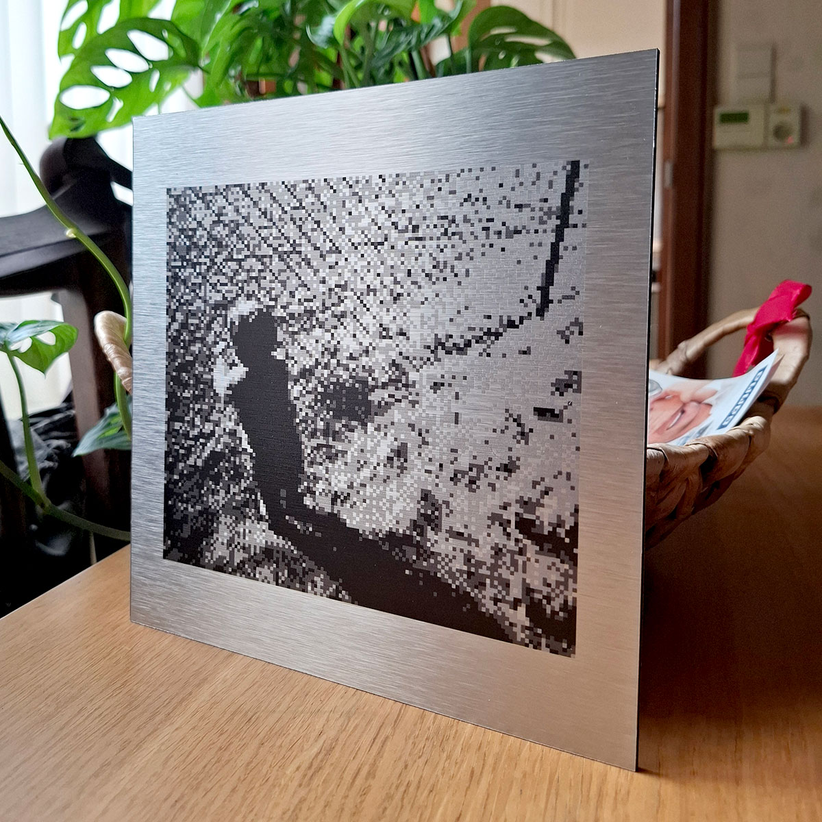 print of a pixel photo on brushed aluminium plate, standing in front of a monstera plant and on a wooden table