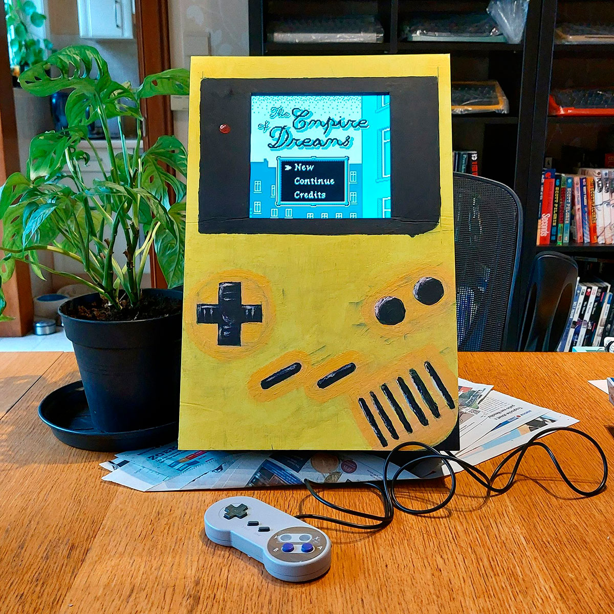 Giant yellow Game Boy with a controller coming out of it, playing my homebrew game Empire of Dreams