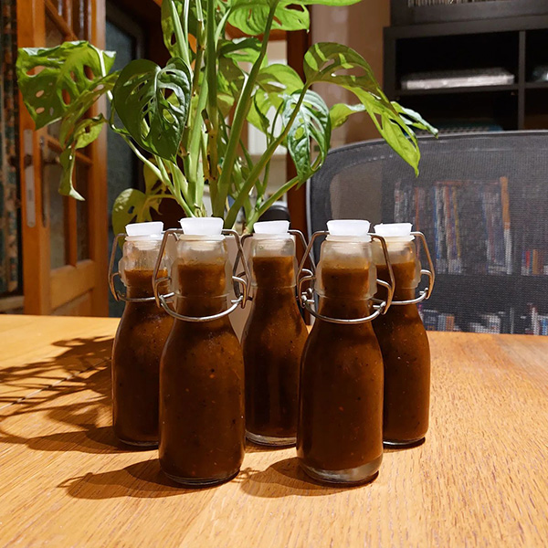 5 glass bottles of dark red hot sauce sat on a wooden table
