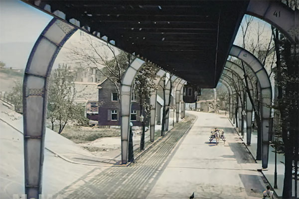 view from a monorail, we see a horse and carriage up ahead and buildings on the left